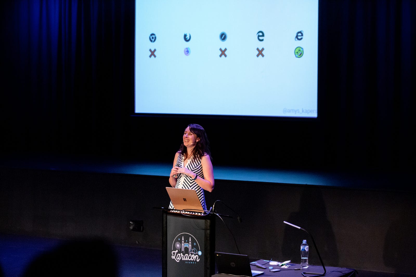 Amy Kapernick smiling at a Laracon Sydney lectern, in front of a projected slide of browser logos