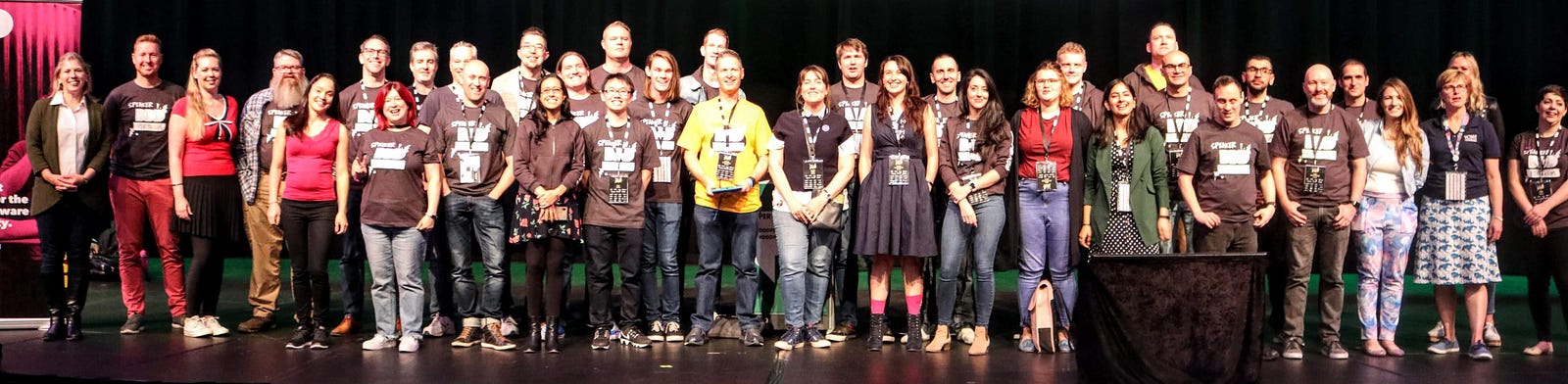 All the speakers of DDD Perth 2019 on the main stage of the conference theatre. They are smiling at the camera.