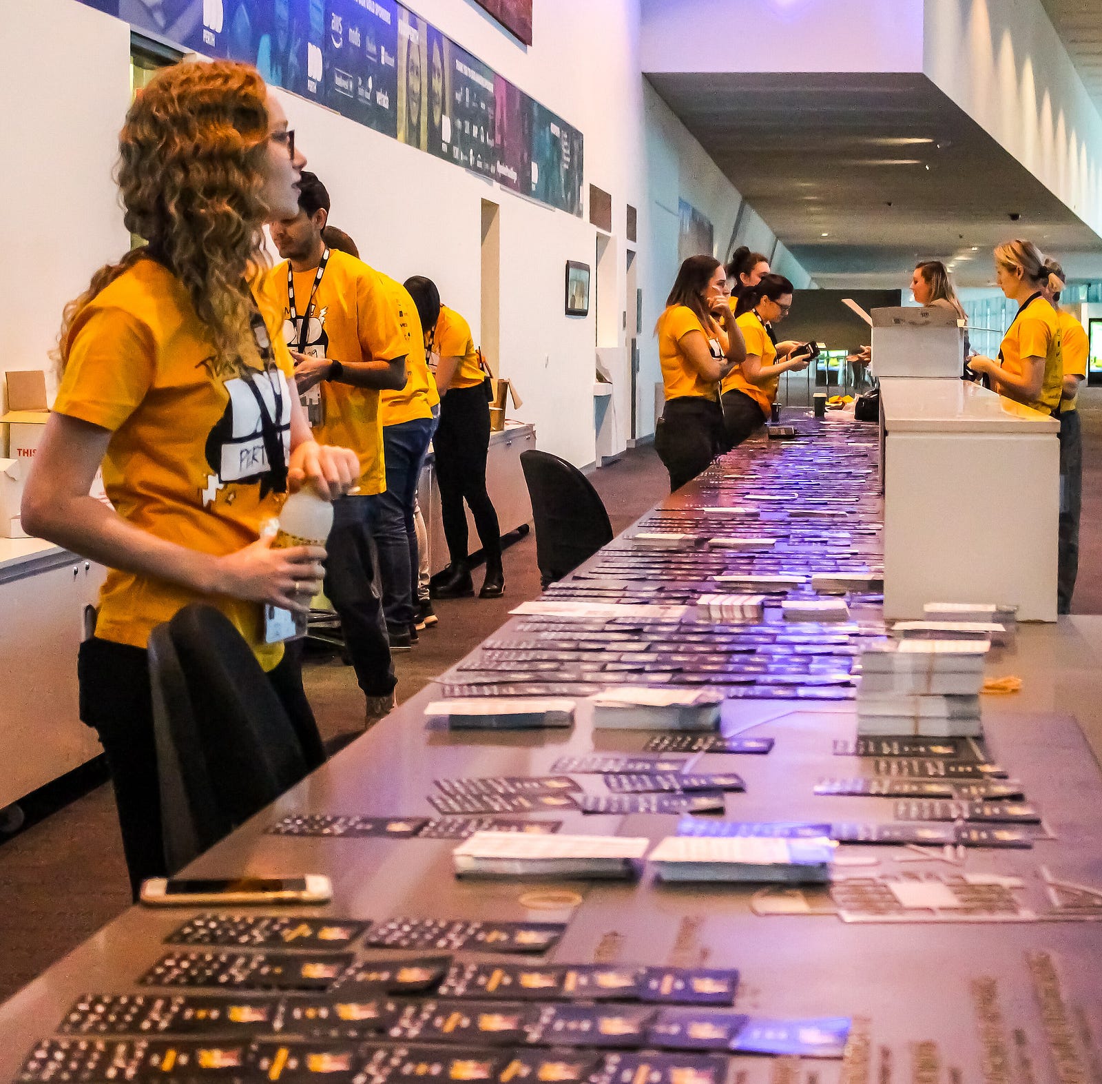 Volunteers in yellow shirts standing around a 6 metre long registration desk with name tags spread out all over it.