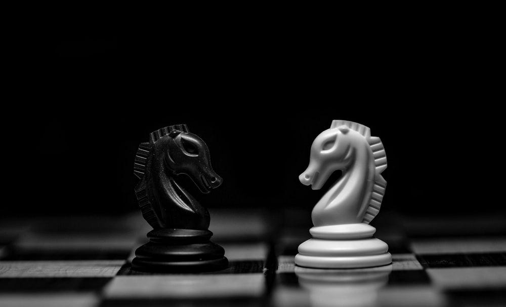 A black and white photo of two chess knights on a chessboard facing each other.